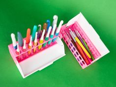 a pink container filled with lots of different colored pens and pencils on top of a green surface