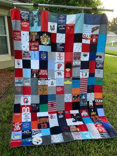 a patchwork quilt is hanging on a clothesline in front of a house with trees and grass