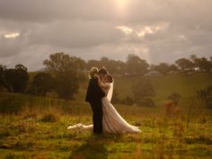 a bride and groom standing in the middle of a lush green field under a cloudy sky