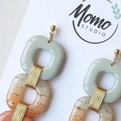 a pair of earrings is shown in front of a card with the logo momo studio on it