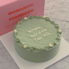 a green cake sitting on top of a table next to a pink card and box