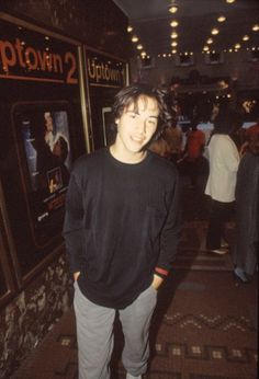 a young man standing in front of a movie poster at an indoor event with people walking around