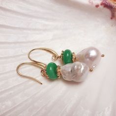 These stunning earrings are a delicate harmony of nature and elegance. At the heart of each piece is a luminous, irregularly shaped baroque pearl, with its organic luster adding a soft, ethereal glow. Stacked gently above the pearl is a smooth, circular green jade bead, offering a striking contrast with its deep, earthy hue. Between the two, a dainty flower spacer, finely crafted, adds a touch of intricate detail, creating a sense of balance and refinement. The entire arrangement is suspended fr Luxurious Earrings, September Birthstone Jewelry, Luxury Earrings, Forever Jewelry, Jewelry Ring Box, Pearl Jewellery Earrings, Men's Jewelry Rings, Evil Eye Jewelry, Stunning Earrings