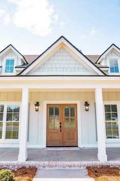 a white house with two brown doors and brick walkway leading to the front door that has windows on both sides