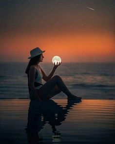 a woman sitting on the edge of a swimming pool holding a glowing ball in her hand