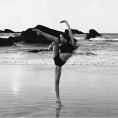 a woman doing a handstand on the beach in front of some water and rocks