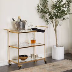 a bar cart with wine glasses and bottles on it next to a potted plant