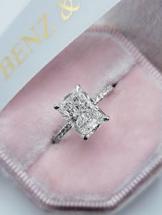 an engagement ring with a princess cut diamond set in a pink velvet box on top of it