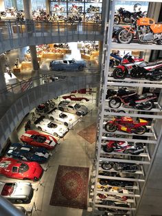 there are many cars and motorcycles on display in the building with people looking at them