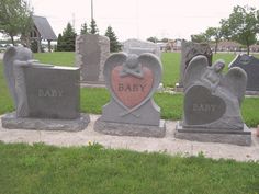 three cement headstones with hearts and wings on them in a cemetery yard, one has a baby heart