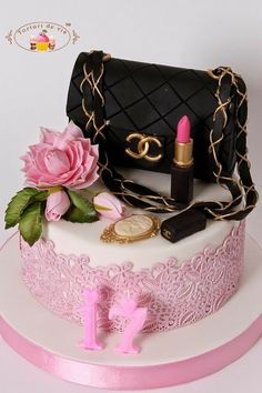 a cake decorated with pink flowers, lipstick and purse on top of a white table