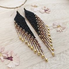 black and gold beaded earrings on a table with flowers in the backgroud