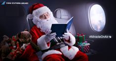 a man dressed as santa claus sitting on an airplane reading a book with stuffed animals around him