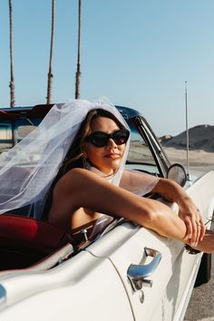 a woman sitting in the back of a white car wearing sunglasses and a wedding veil