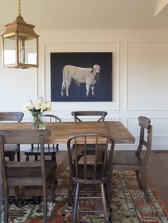 a dining room table with chairs and a cow painting on the wall behind it,