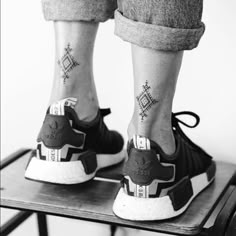 black and white photo of someones feet with tattoos on their ankles, standing on a stool