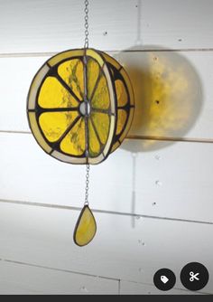 a stained glass lemon slice hanging from a hook on a white wall with water drops