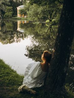 a woman sitting next to a tree near a body of water