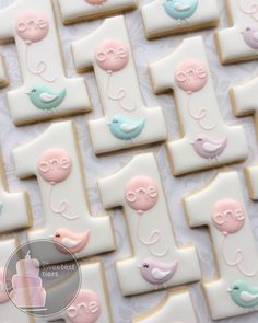 decorated cookies are arranged in rows on a white tablecloth with pink, blue and green decorations