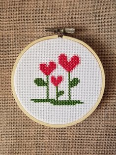 a cross stitch pattern with three red flowers in the shape of hearts on a piece of burlock