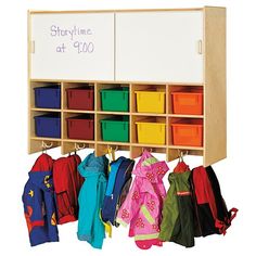 a wooden coat rack filled with lots of coats and bins next to a whiteboard