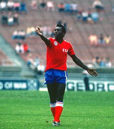 a soccer player in red and blue is on the field with his arms out wide