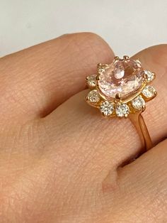 a woman's hand holding a ring with an oval shaped pink diamond in it