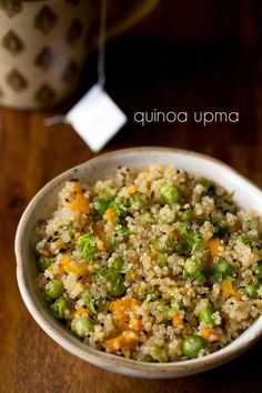 a bowl filled with rice and vegetables on top of a wooden table next to a cup