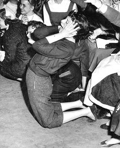 an old black and white photo of people sitting on the ground with their arms around each other