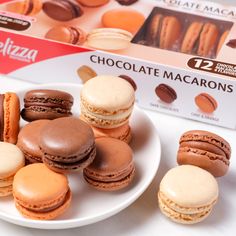 assorted chocolate macaroons on white plate next to box of macaroons