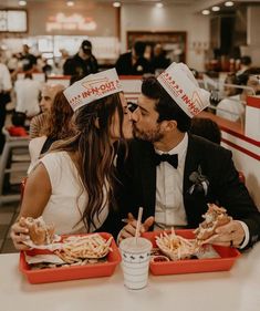 a man and woman sitting at a table with food in trays on their heads