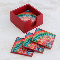 three colorful coasters in a red box on top of a white surface with the lid open