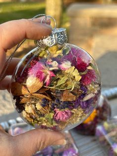 a hand holding a glass ornament filled with flowers