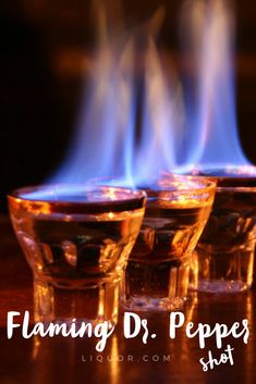 three glasses filled with liquid sitting on top of a wooden table next to blue flames