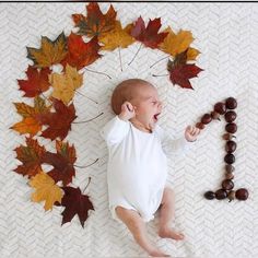 a baby laying on top of a white blanket next to autumn leaves and bead necklaces