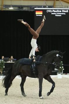 a person riding on the back of a black horse while holding onto it's leg