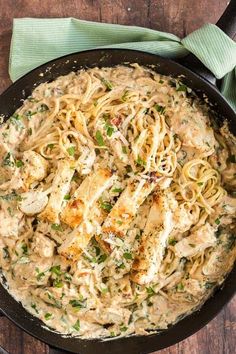 a skillet filled with chicken and pasta on top of a wooden table next to a green napkin