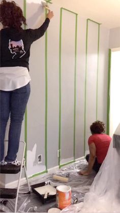 two women are painting the walls in a room that is being remodeled with green tape