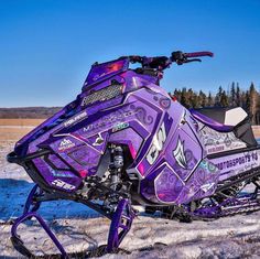 a purple and black snowmobile parked on the side of a road in the snow