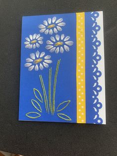 a blue card with white daisies and yellow ribbon on it, sitting on a table