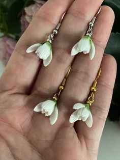 three white flowers are attached to gold chain earwires in the palm of someone's hand