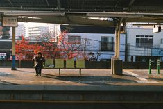 a woman is standing on the platform waiting for her train