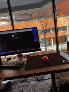 a desk with a keyboard, mouse and monitor on it in front of a large window