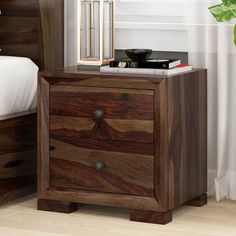 a wooden night stand with two drawers and a mirror on top of it, next to a bed