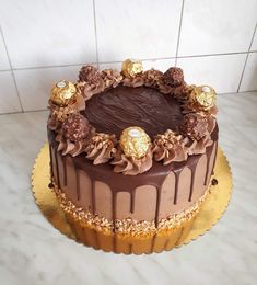 a chocolate cake sitting on top of a counter next to a white tile wall with gold decorations