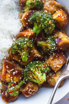 a white plate topped with meat and broccoli covered in sesame seeds next to rice