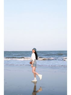 a woman walking on the beach with her hat in her hand and shoes in her other hand