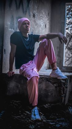 a man sitting on top of a wall wearing pink pants