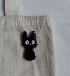 a black cat brooch sitting on top of a white cloth covered tote bag