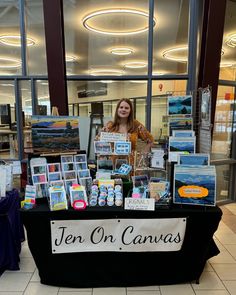 a woman standing behind a table with paintings on it in front of a glass window